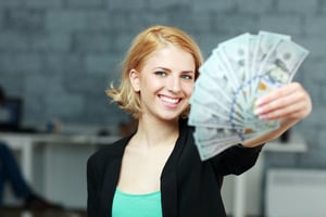 Young happy businesswoman holding bills of dollars in office